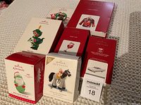 Photo of 8 Hallmark Keepsake ornaments in original boxes on a beige background.