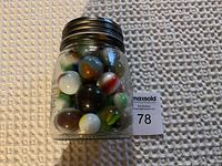 Glass jar with metal lid filled with large multicolored marbles, shown upright.