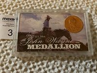 Front view of John Wayne medallion in acrylic display case showing gold medallion with profile of John Wayne and color card background.