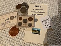 Image showing assorted foreign coins including Franklin Mint collector coin in protective holder, coins in display case, round coin in capsule, large copper-colored coin, Icelandic collectors' coin and postage stamp with paper holder.