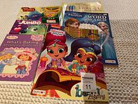 Photo of coloring and activity books featuring Strawberry Shortcake, Shimmer and Shine, and Frozen, along with Trolls jumbo crayons and Crayola colored markers on a white surface.