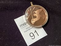 Photo showing the pendant in its clear protective case on a dark fabric background with a lot number tag.