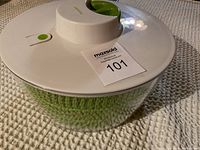 Top and side view of salad spinner showing white lid with green handle and green button, clear bowl with green basket inside.
