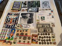 Overview of lot on textured white surface including silver bar, coins, cards, photos, stamps and covers