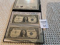 Two U.S. one-dollar Silver Certificates displayed in protective sleeves with informational backing showing details of the certificates.