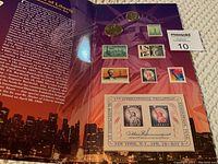 Set of commemorative coins and stamps themed around Statue of Liberty on a colorful backdrop with informational text
