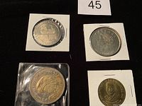 Four tokens displayed on black background, three housed in white holders, one in plastic sleeve.