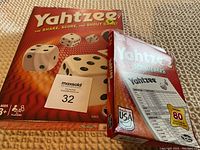 Photo of unopened Yahtzee game box and unopened Yahtzee score cards pack on textured surface.