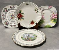 Four porcelain plates displayed, including Royal Albert Poinsettia cake plate, additional floral cake plates, and cherry blossom dinner plate.
