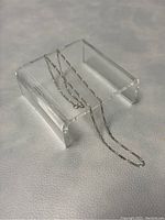 White gold chain draped over clear acrylic display stand