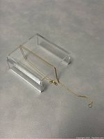 Two gold chains draped over clear acrylic stand on white background