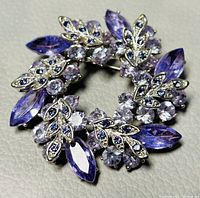 Front view of vintage silver-tone brooch with purple and clear crystals arranged in a circular wreath shape.