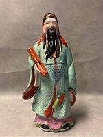 Front view of the porcelain figurine with detailed facial features, robe, and scroll.