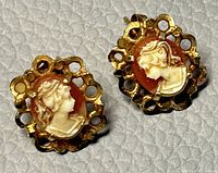 Close-up front view of pair of cameo stud earrings showing carved female profile and gold filigree frame