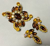 Brooch and earrings laid flat to show overall look, color, and design details of the crystals and gold-tone metal