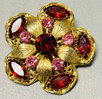 Close-up view of the filigree floral brooch showing red marquise-shaped crystals and pink round crystals with gold-tone metal leaves.