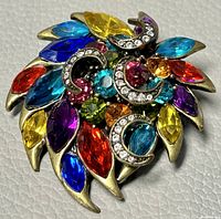 Front view of vintage metal and crystal brooch with colorful marquise and round crystals and rhinestone crescents on gold-tone metal leaf base.