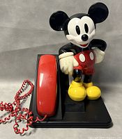 Front side view of the vintage Mickey Mouse telephone showing the red handset, coiled cord and Mickey Mouse figure on black base.
