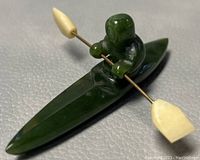 Close-up side angle of green jade Inuit figure in kayak with bone paddle blades on metal rod
