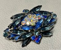 Close-up image showing the front of the brooch with blue marquise and round crystals surrounding a large central faceted crystal cluster.