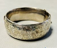Close-up photo showing the sterling silver bracelet's wide band with detailed floral etching and visible patina.