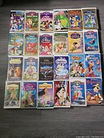 Image showing the front of 24 Disney VHS cases arranged in 4 rows with 6 movies each. Classic animated movies like The Little Mermaid, Mulan, Dumbo, Pinocchio, Beauty and the Beast visible.