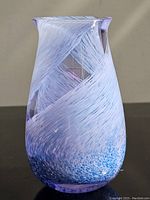 Front and side view of blue and white art glass vase with swirling design and speckled base on black reflective surface.