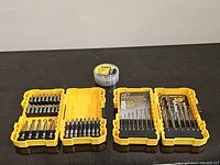 Top-down view showing four yellow plastic DeWalt drill bit cases open and a small clear container with yellow DeWalt lid containing small parts or bits.