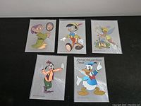Overview photo of five Disney Dufex foil postcards arranged on black fabric.
