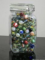 Clear glass jar with metal clasp filled with assorted colorful vintage marbles