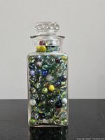 Front view of glass jar filled with assorted marbles, showing jar shape and stopper lid.