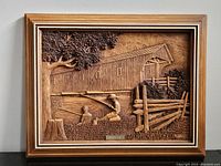 Frontal view of a wooden carved wall art depicting a covered bridge, children fishing by a river, tree and fence detail, all carved in wood.