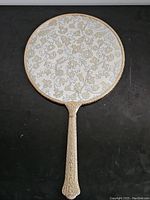 Top view of the ornate brass hand mirror showing the detailed floral pattern on the back and the decorative handle.