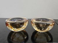 Side view of two Kosta Boda votive holders showing clear glass with embedded swirls in amber and smoky brown.