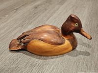 Side profile of signed wooden duck carving showing wood grain, body and head details, tail damage visible