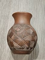 Front and side views showing hand-carved geometric patterns and the flared neck of the brown pottery vase.