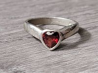 Close-up photo of the silver ring's top showing heart-shaped red faceted gemstone set in bezel on a silver band.