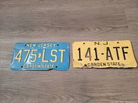 Two New Jersey license plates, one blue with yellow lettering and one yellow with black lettering, shown side by side on a wooden floor.