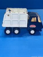 Side view of vintage Tonka garbage truck with dark blue cab and white rear container, showing some paint wear.