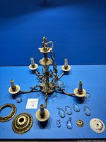 Full view of bronze chandelier with five arms, plastic candle sleeves on each arm, and several detached parts including hanging crystal prisms and decorative bronze pieces laid out separately.