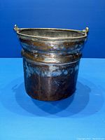 Overall front and side view of the antique copper pot showing the cylindrical shape, dark patina, and ribs on the body.