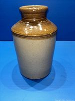 Front view of antique two-tone stoneware crock showing brown glazed neck and beige body.