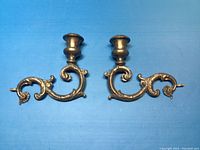 Pair of silver-plated antique style wall sconces for holding candles, shown against blue background.