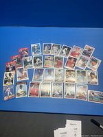 Photo showing 36 assorted baseball cards laid out in rows on a blue background, visible player images and card details.