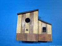 Wooden bird house with two compartments, circular entrance hole, and small window, shown from front.