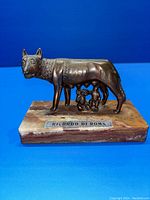 Front angle of copper Capitoline Wolf statuette on marble base with inscription plate