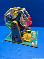 Front side view of the colorful vintage FP Ferris wheel toy with multiple gondolas, painted base, and small figure attendee.
