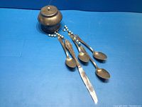 Silver plated mobile consisting of three hanging teaspoons and one butter knife attached to a rounded top piece.