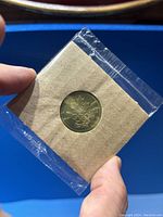 Close-up photo of a single 2002 Olympic hockey token in sealed packaging with clear plastic and brown backing card, showing embossing detail of Olympic rings and maple leaf.