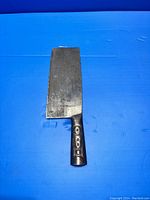 Full view of the vintage steel cleaver on a blue background, showing entire blade and handle.